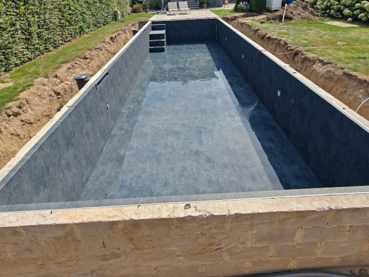 Rechthoekig betonnen zwembad in aanleg, met grijze bekleding en open kuip in tuinomgeving.